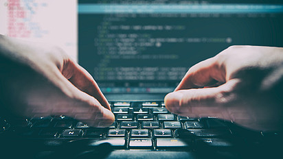 Hände auf Computertastatur, Bildschirm im Hintergrund